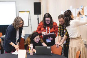 A group of people working together huddled around a laptop computer