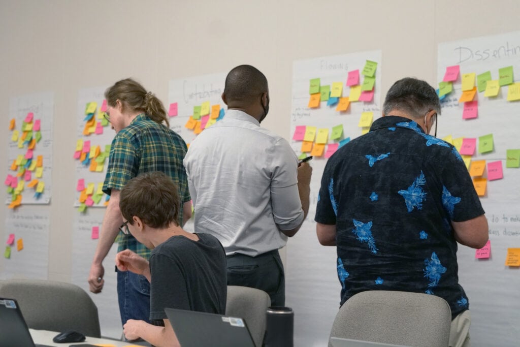 People examine and add sticky notes to posters on a wall